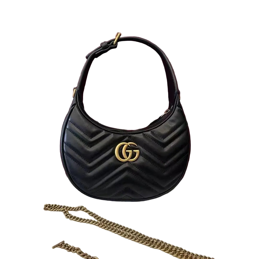 A black quilted Gucci shoulder bag with a gold interlocking GG logo, displayed in front of a burgundy Gucci box on a white dust bag with a gold chain strap.