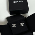 Chanel double-C logo stud earrings with sparkling crystals, presented in an open black Chanel box with the brand's signature box lid visible in the background.