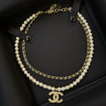 A double-strand Chanel necklace featuring white faux pearls and gold-tone chains, with a gold-tone interlocking CC logo pendant, displayed inside a black presentation box.
