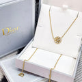 A gold necklace with a circular starburst pendant displayed in an open white Dior jewelry box, alongside the Dior-branded packaging.