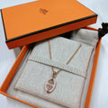 A gold-tone necklace with a rose gold-toned oval pendant displayed inside an orange Hermes gift box with a patterned fabric insert.